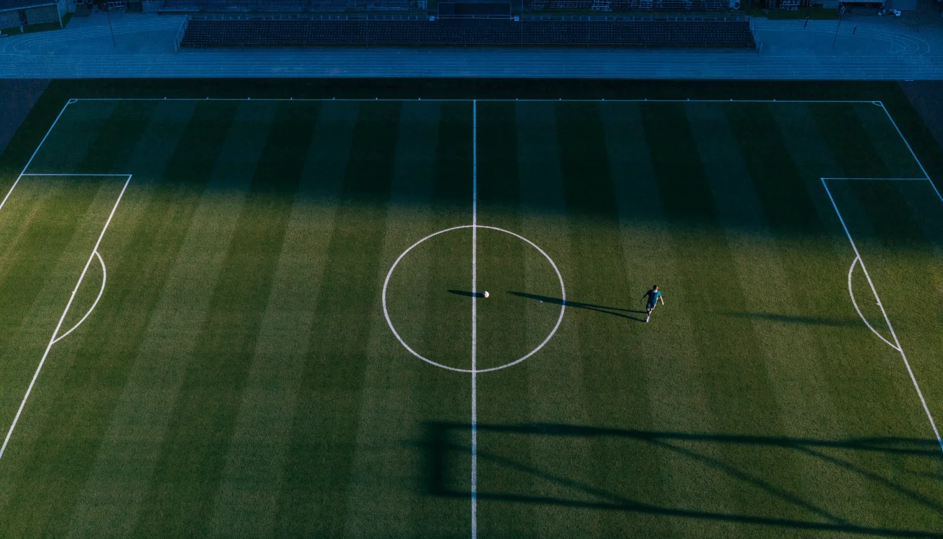 Ein Fussballplatz von oben gesehen, die Linien bilden ein helles Muster auf dem Rasen, Drohnenperspektive in der Morgendämmerung.