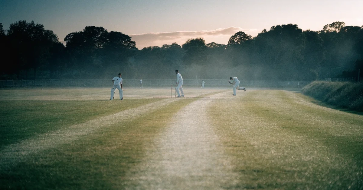 Ein ovales Cricketfeld mit gemähtem Rasen und hellem Mittelstreifen am frühen Morgen, Nebel zwischen den Bäumen am Rand