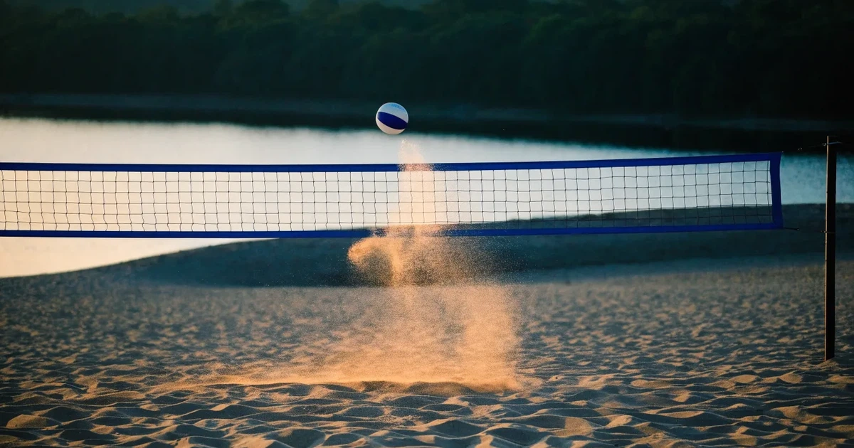 Ein Volleyball liegt im Sand eines Beachplatzes, zwischen zwei Pfosten ist ein Netz gespannt, tiefe Abendsonne wirft lange Schatten.