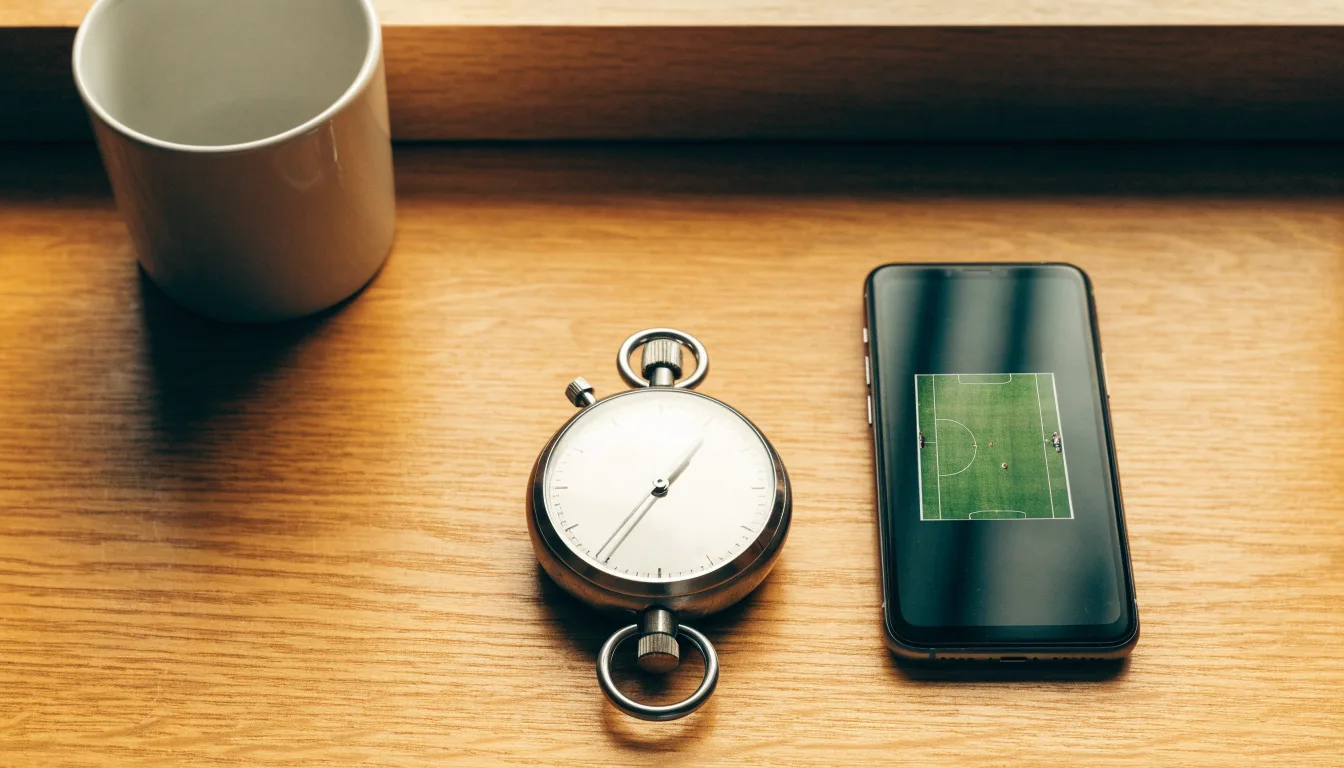 Eine Stoppuhr und ein Smartphone mit dunklem Display liegen nebeneinander auf einem Holztisch, weiches Fensterlicht
